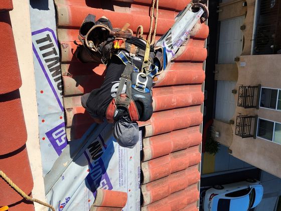 NRG Roofing crew tied off resetting tile above a condo unit, Oxnard HOA roof repair