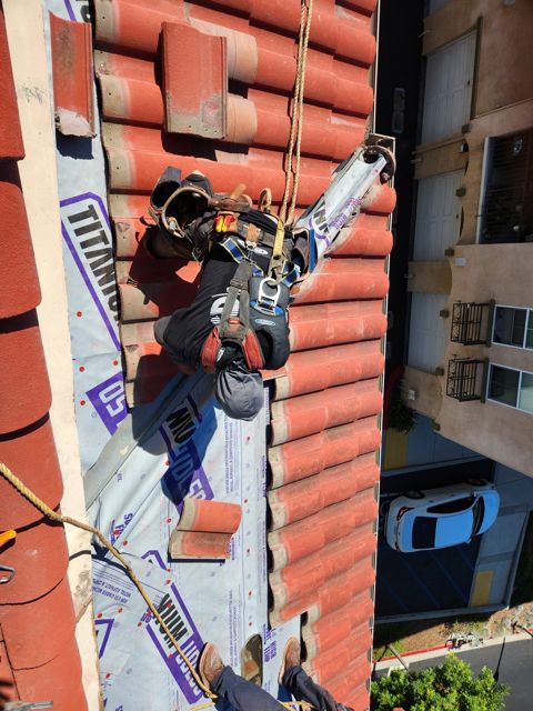 NRG Roofing crew tied off resetting tile above a condo unit, Oxnard HOA roof repair