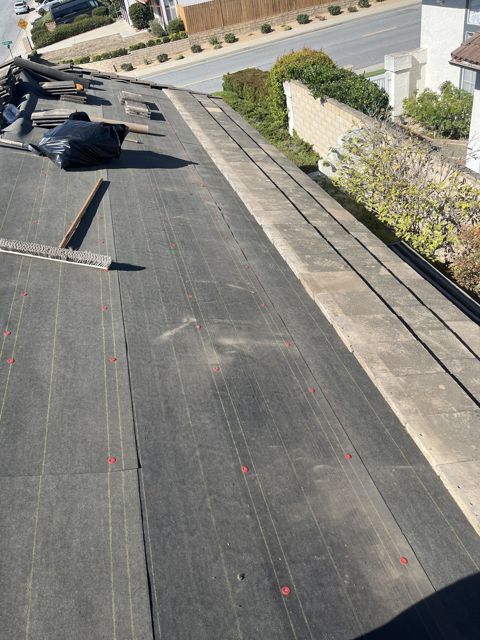 NRG Roofing crew installing new tile underlayment across a lifted facet, original tile stacked for re-set, Ventura